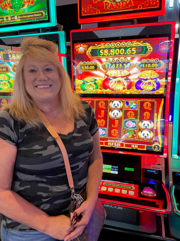 Julie S. standing in front of machine with $9,015.65 jackpot win.