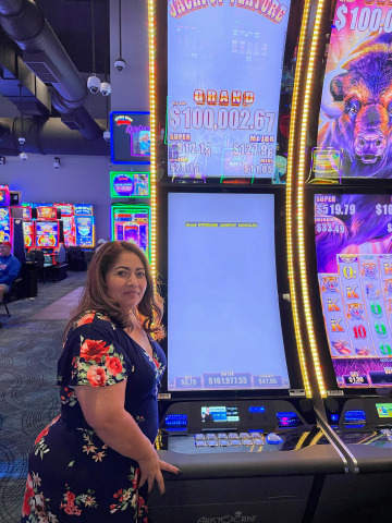 Maria P. standing in front of machine with $161,977.53 jackpot win.
